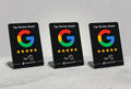 Three black acrylic Google review display signs on small stands, each showing the Google G logo, five gold stars, and the text 'Tap, Review, Simple' on a light gray background.