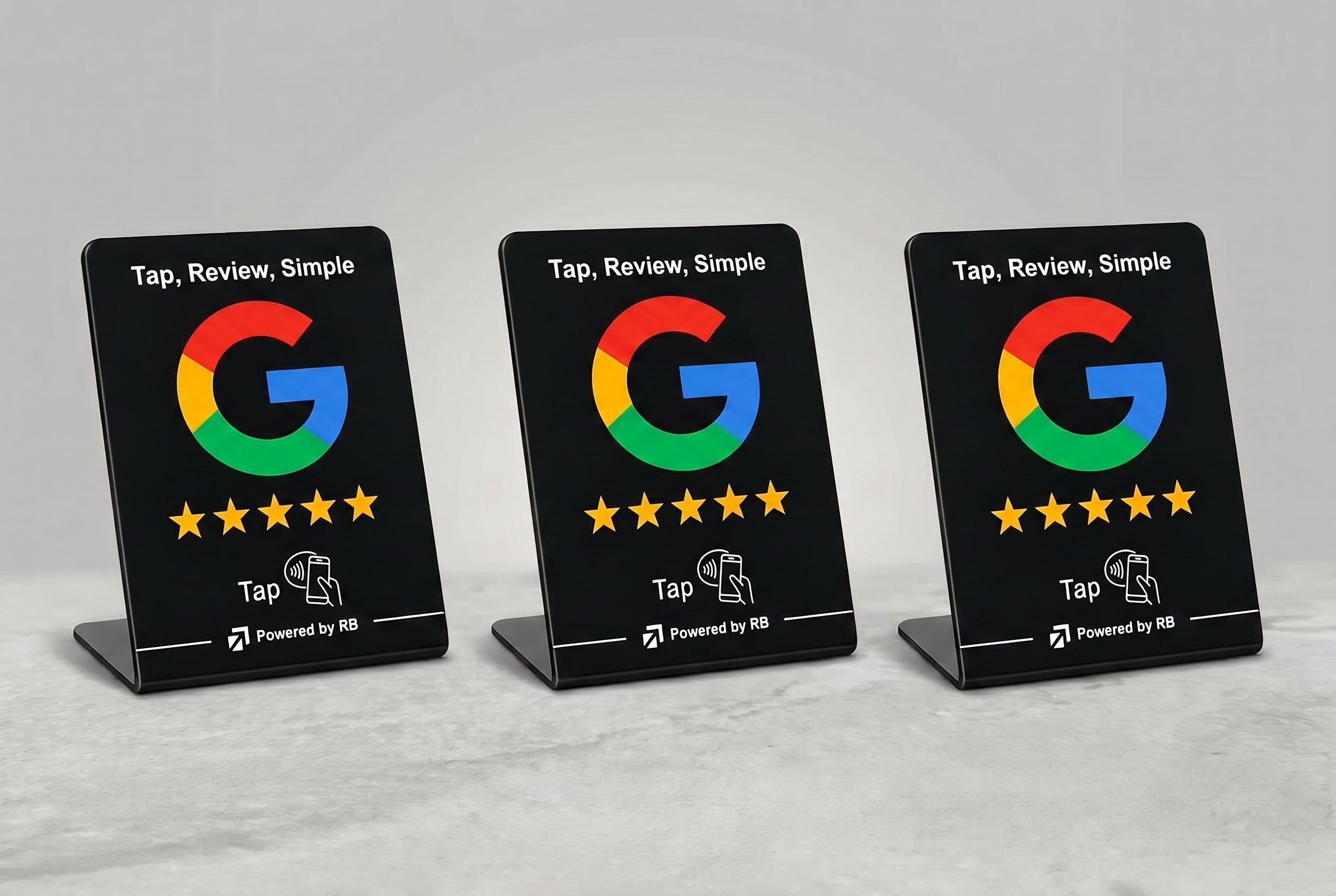 Three black acrylic Google review display signs on small stands, each showing the Google G logo, five gold stars, and the text 'Tap, Review, Simple' on a light gray background.